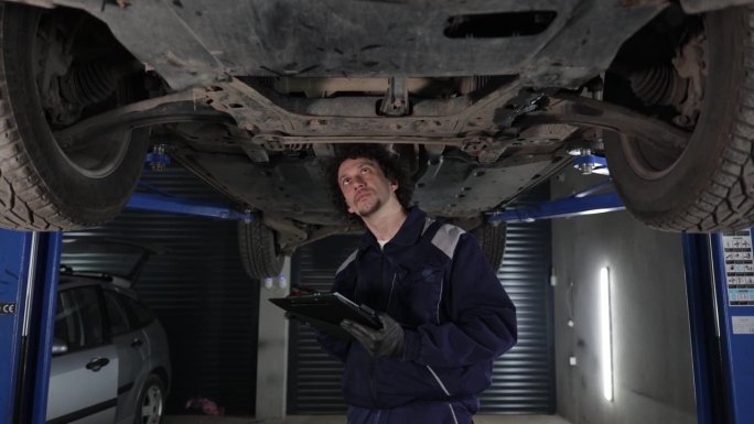 专业修理工戴着手套，在车底使用棘轮。现代洁净车间