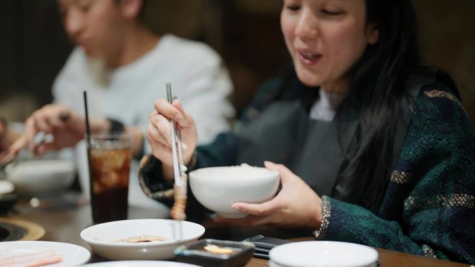 亚洲妇女拿着筷子和
在传统的韩式烧烤餐厅吃着韩式烤肉。