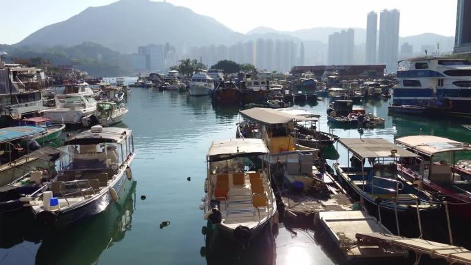在香港鲤鱼门，多艘停泊在避风塘内的船只的正面视图，背景是山和建筑物。