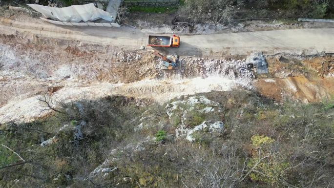 放大无人机拍摄的滑坡后，挖掘机将泥土和碎石装上卡车进行清理的画面