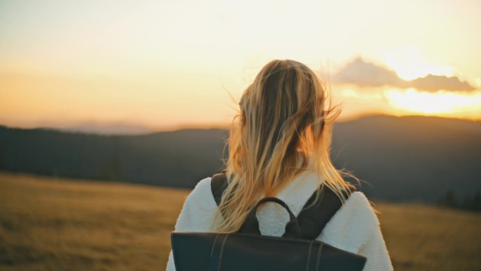 年轻的金发女郎背着双肩包在日出时欣赏山景