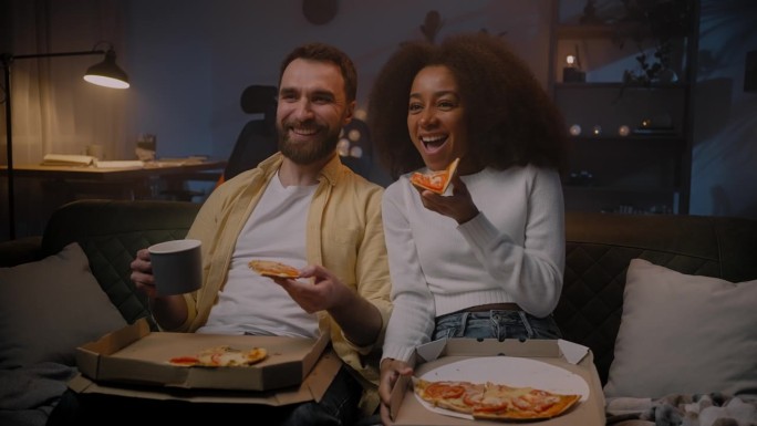 两个相爱的人在空闲时间坐在沙发上看电视剧，吃披萨