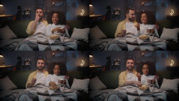 两个相爱的人在空闲时间坐在沙发上看电视剧，吃着爆米花