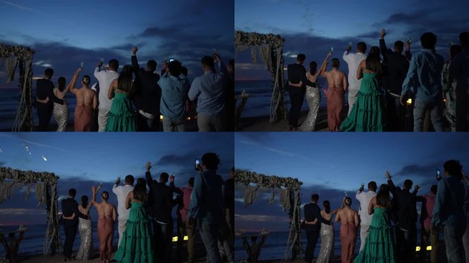 新娘和新郎在海滩上与婚礼客人一起看烟花