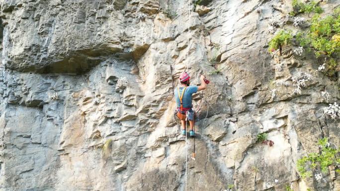 使用凿岩机和旋锤在攀绳上开辟新的攀爬路线的鸟瞰图。登山者戴着红色的头盔。