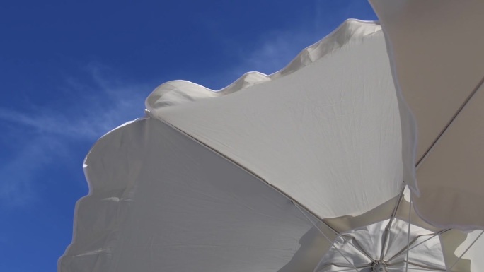 白色沙滩伞的褶边在蓝天上随风飘动