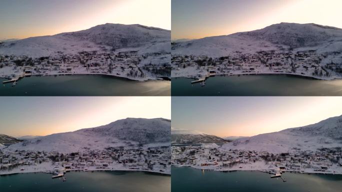日出时，海边白雪覆盖的村庄，厄斯峡湾的地平线上有温暖的光线