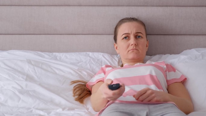 紧张的女人躺在床上看电视。惊恐发作的女人