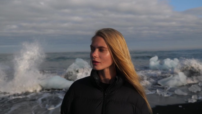 美丽的金发女郎在冰岛的钻石海滩探险，海滩上有大块的冰块
