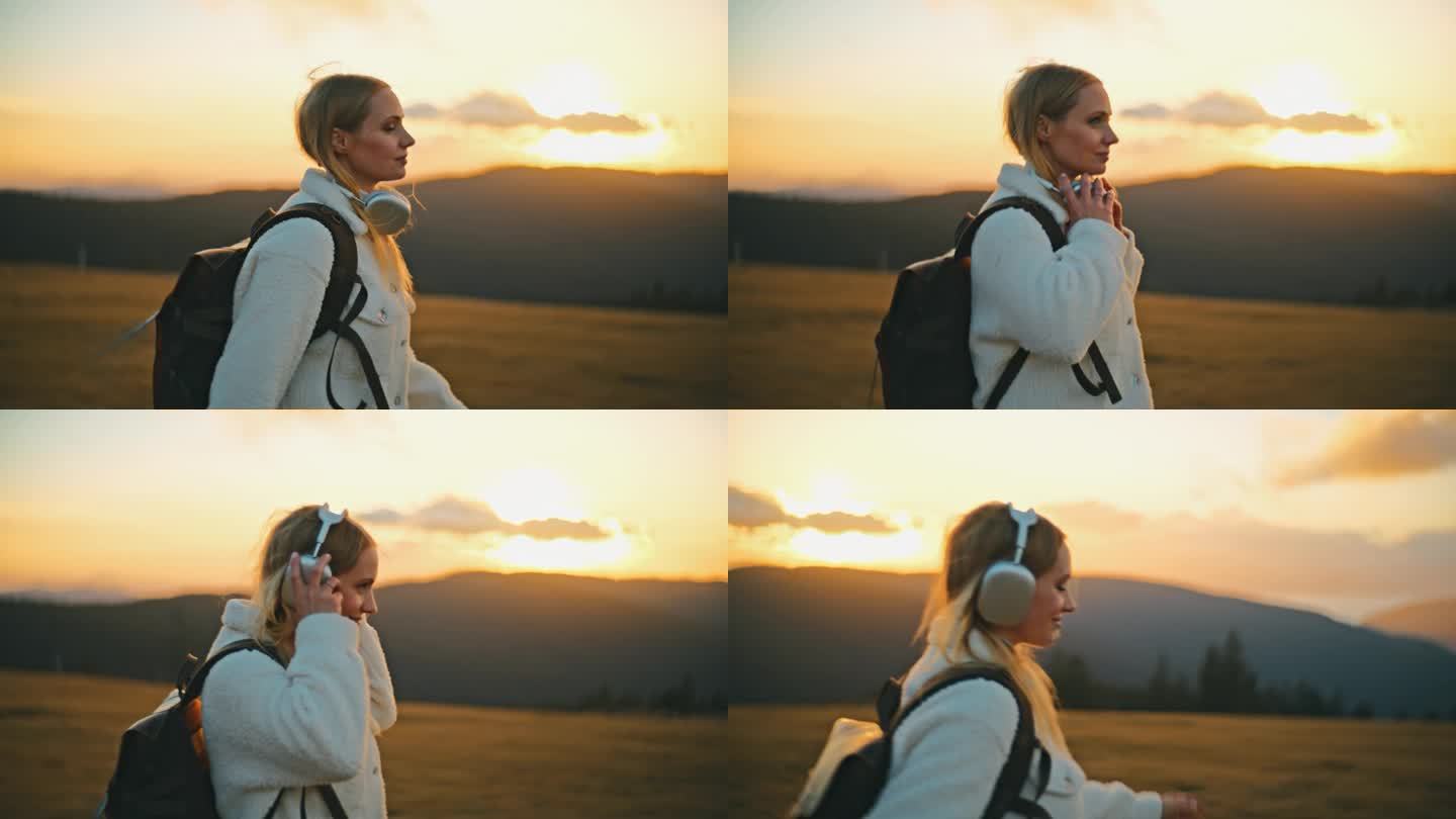 慢镜头:日出时，戴着耳机的年轻女子在山间徒步旅行