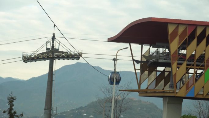 索道的小屋沿着缆索上升到城市上方，以山脉为背景。悬挂架沿滚子接头移动。山地缆车