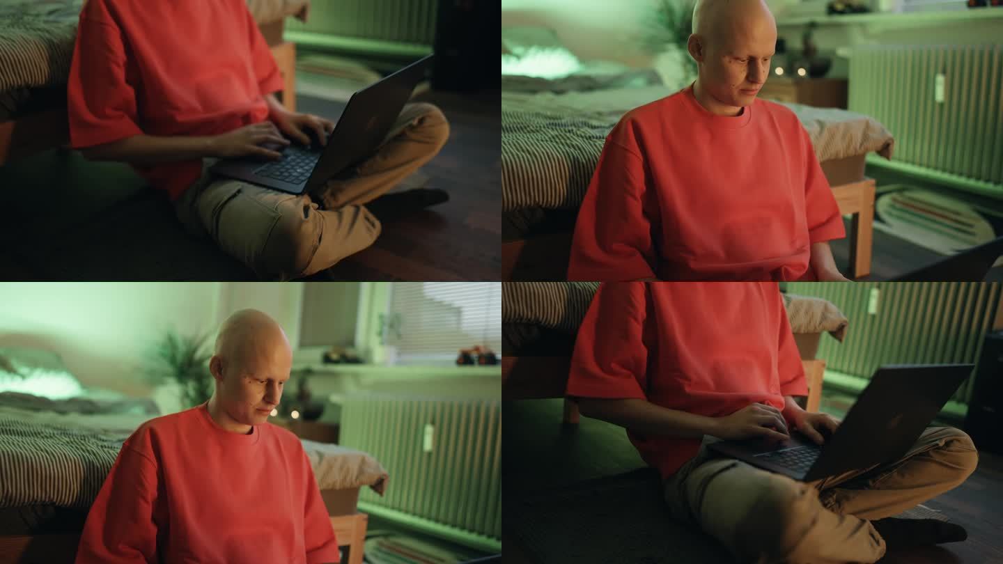摄于家中卧室，年轻的秃顶癌症患者坐在地板上用笔记本电脑工作的特写