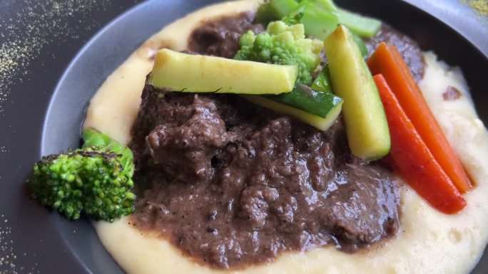 热气腾腾的食物炖牛肉配上煮熟的蔬菜和土豆泥放在盘子里