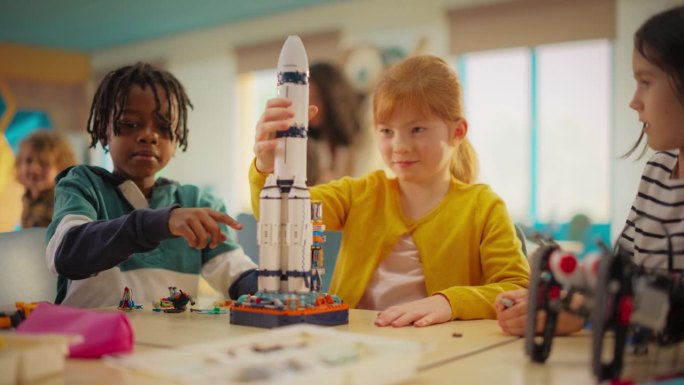 不同的小学生在课堂上建造太空火箭模型。女孩正在安装飞船的顶部并完成项目。孩子在成功完成目标后击掌