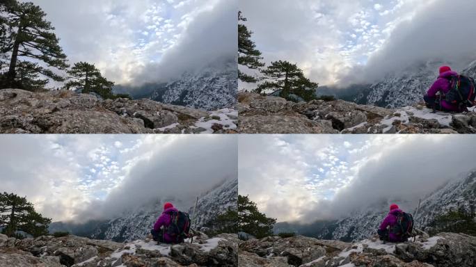 一位女登山者坐在岩石上，眺望着高山的风景和峰顶。