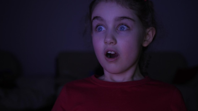 看电视时给孩子画像。害怕的女孩在客厅看电视。沉迷电子游戏娱乐。在黑暗的房间里，孩子们在电视或电脑上看