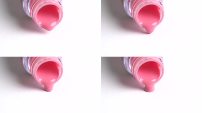 粉红色的唇膏从翻倒的瓶子里流出。白色背景上的珊瑚色唇彩。装饰性化妆品广告概念
