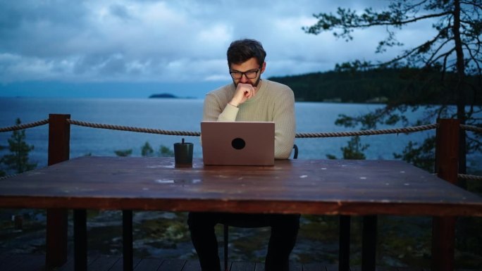 一个人在晚上用笔记本电脑工作，独自坐在生态酒店的露天露台上