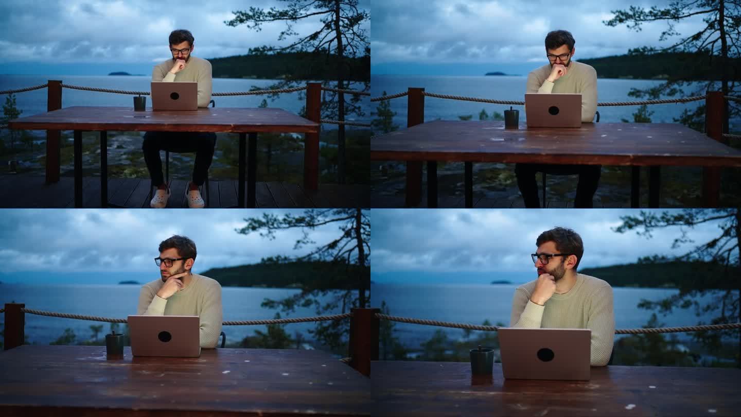 一个人在晚上用笔记本电脑工作，独自坐在生态酒店的露天露台上