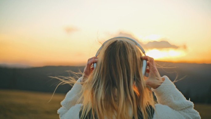 日出时戴着耳机在野外徒步旅行的年轻女子
