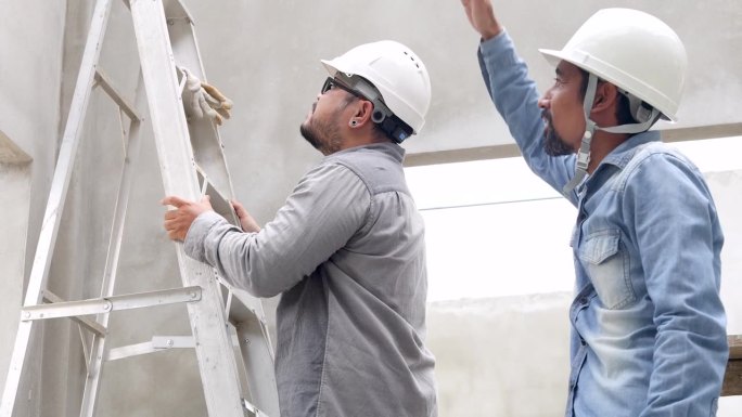 两个工程工人男爬梯子，讨论，解决问题施工检查现场比较图纸文书，印度中年工头站在一起建筑员工