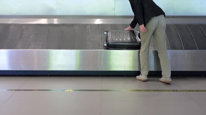 一名男子从机场行李领取大厅的行李传送带上取下他的手提箱