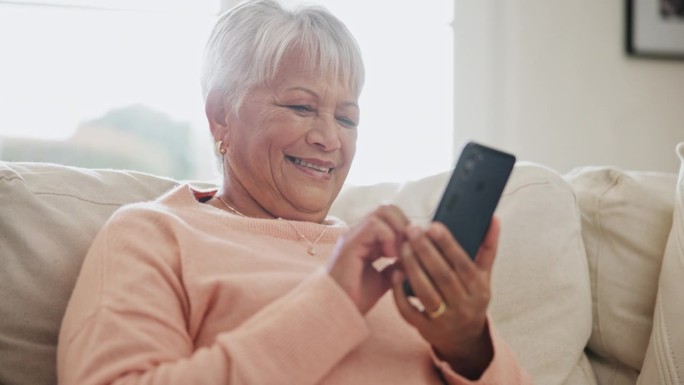 老年女性，客厅沙发上的智能手机和社交媒体，表情包或科技。退休，快乐或享受退休放松，移动应用程序或短信