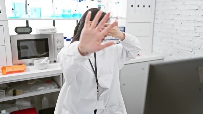 惊慌失措的年轻中国女科学家在实验室里用手捂着眼睛，做着停止的手势。她的表情传达出一种消极的、令人担忧
