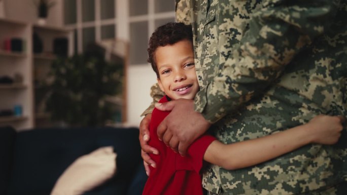 男孩抱着身穿军装的爸爸，微笑着迎接父亲的归来