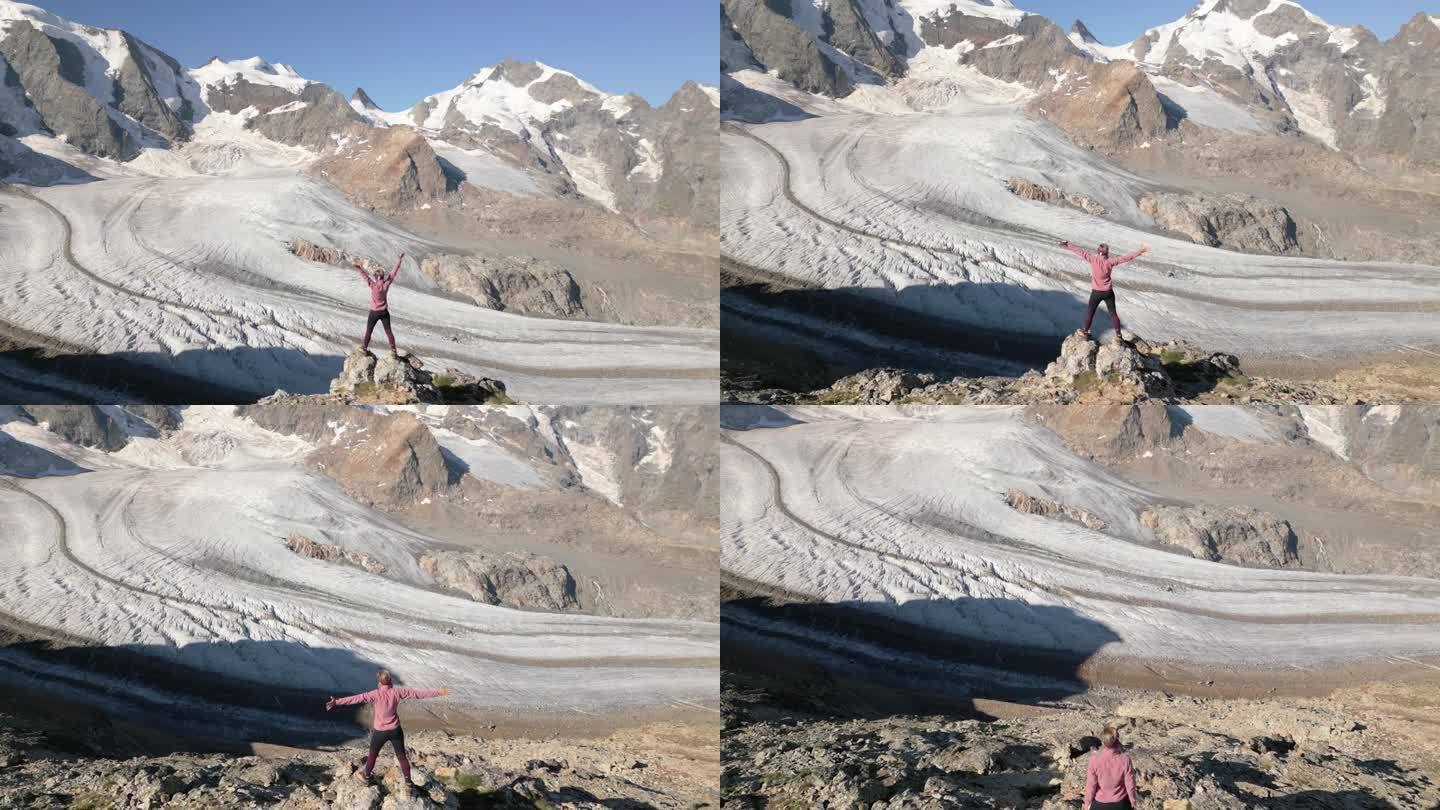 无人机鸟瞰图，女登山者站在冰川上，双臂张开