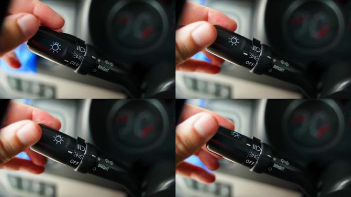 一只手在切换汽车的前灯模式，特写。汽车内部的远光灯和行车灯开关