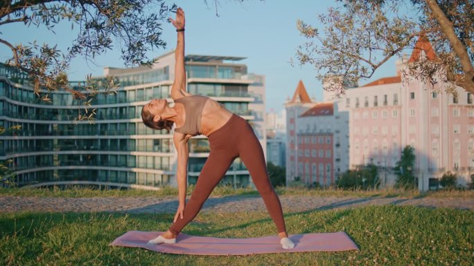 在阳光绿色公园做弯身瑜伽的女人。女运动员做三角体式