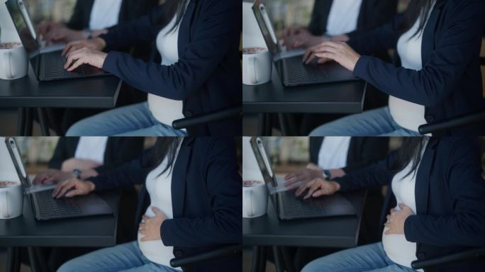 一个孕妇坐在椅子上，在户外工作时摸着肚子的特写