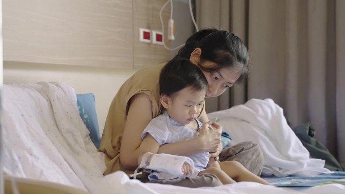 可爱的亚洲孩子感染了病毒，他照顾和使用体温计测量体温由他的母亲接受抗生素药物和输液生理盐水在医院等待
