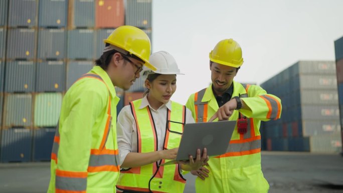 一组工业工程师，身穿安全制服，头戴头盔，手持笔记本电脑在集装箱码头工作。货物运输进出口业。物流航运堆