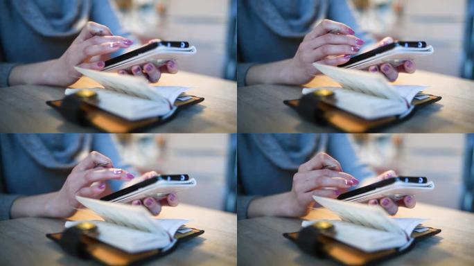 一位女士一边看笔记本一边操作智能手机的手