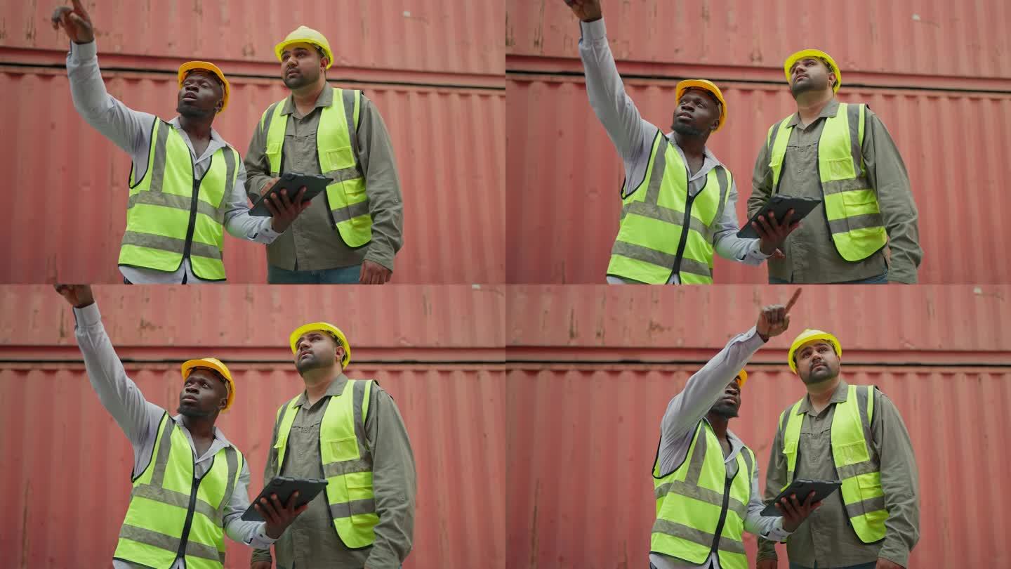 两名身穿安全制服的工业工人在仓库一起检查平板上的容器。黑人男性主管和印度工业工程师在平板电脑上交谈。