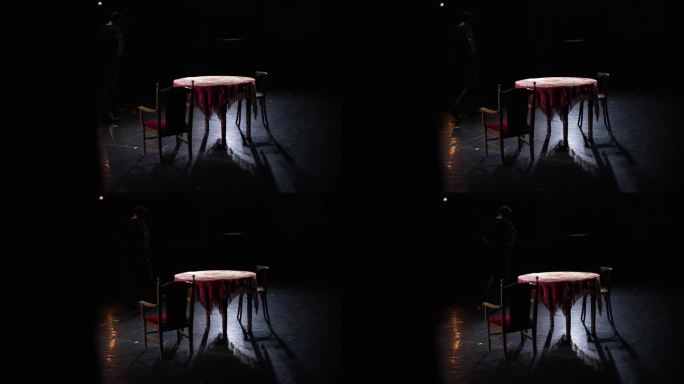 演员走过舞台，旁边是一张旧桌子和椅子。