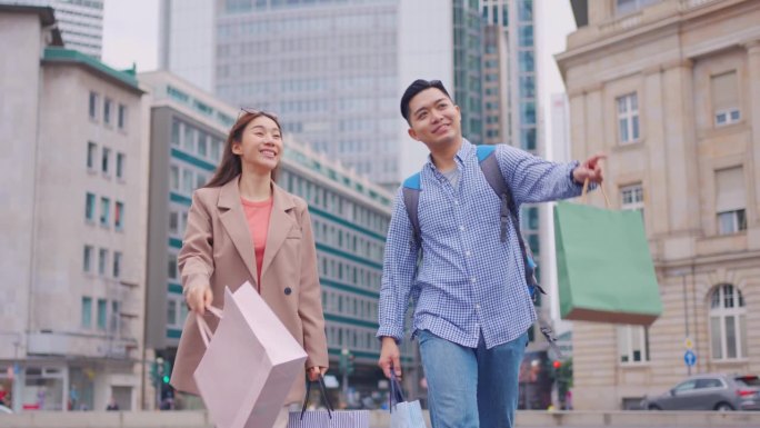 亚洲青年男女在百货公司户外购物。迷人的情侣提着购物袋，幸福地走在一起，在商场商场中心享受购物。