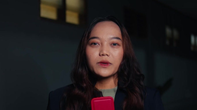 一个棕色头发、黑色外套的亚洲女人像记者一样对着镜头说话