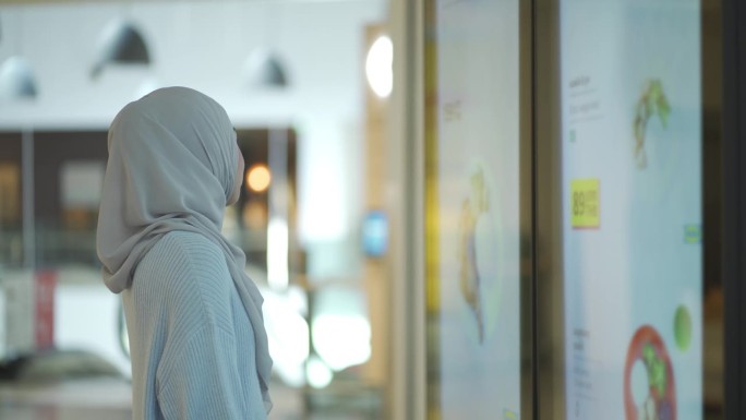 年轻的穆斯林妇女看液晶电视墙的特写