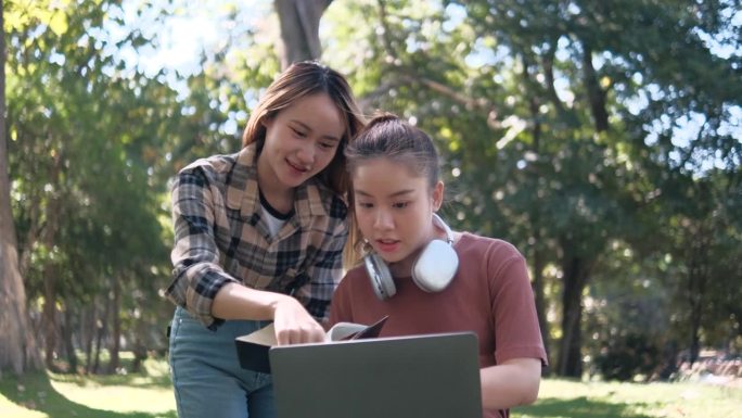 两名女学生坐在大学校园的草地上一起工作和学习考试