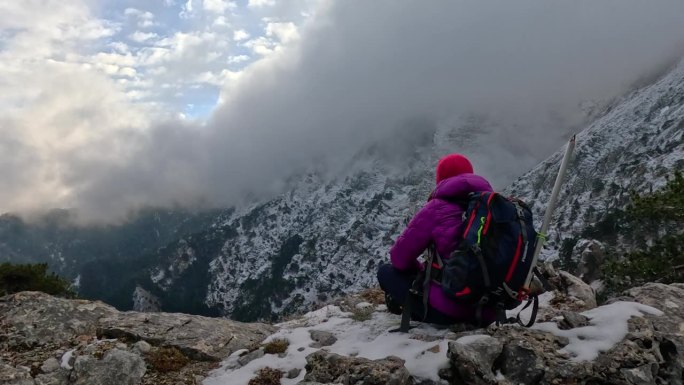 一位女登山者坐在岩石上，眺望着高山的风景和峰顶。
