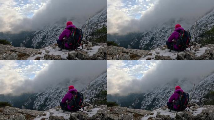 一位女登山者坐在岩石上，眺望着高山的风景和峰顶。