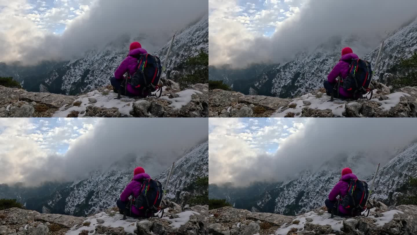 一位女登山者坐在岩石上，眺望着高山的风景和峰顶。