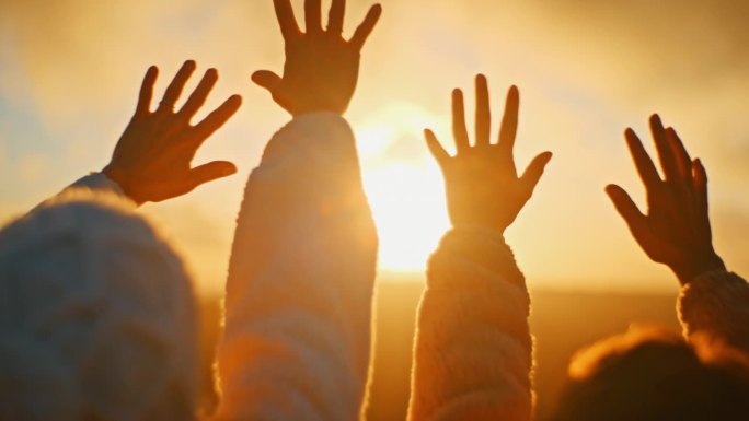 在日出时，年轻的女人举起双手朝向金色的阳光