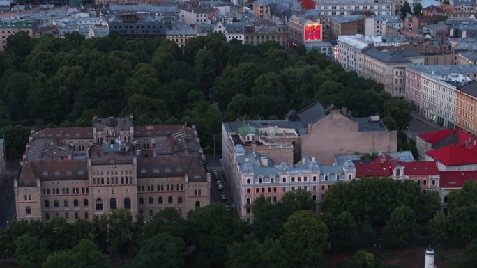 鸟瞰图:公园里被大树环绕的大型宫殿。向上倾斜显示黄昏的城市景观。里加,拉脱维亚