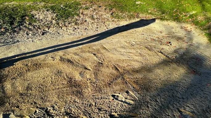 在一个阳光明媚的日子里，高尔夫球场上，一个高尔夫球手用他的高尔夫球杆楔子成功地在沙坑里打高尔夫球的影