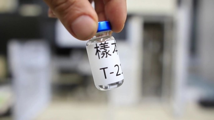 在分析化学实验室里，一名男子拿着一个小瓶，里面的液体用汉字标记为样品