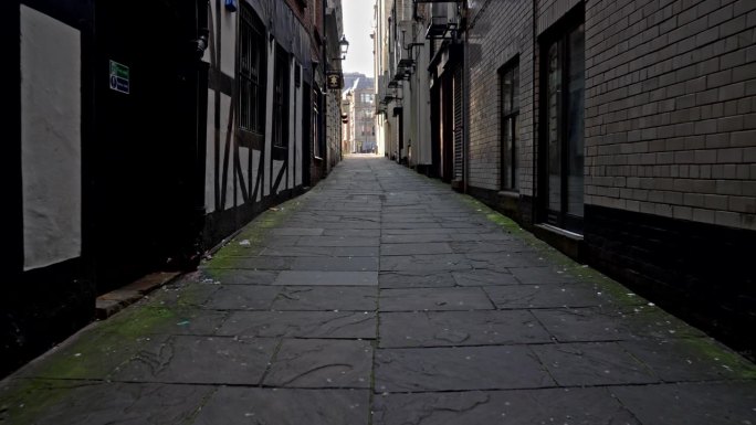 2023年5月20日，英国利物浦:手持摄像机走在一条黑暗、阴暗的石头小巷里，朝着前方明亮的入口走去